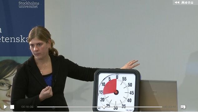 Erika föreläser med handen på en klocka