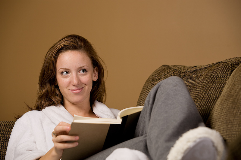 Kvinna sitter i soffan med benen uppe och en bok i knät
