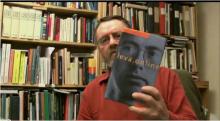 Torbjörn Lundgren sitter framför en bokhylla och håller upp en bok